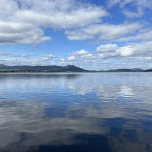 A photograph taken from the bank of the Dornoch Firth with far-reaching veiws across the calm water. The sky is blue with white clouds and across the water you can see the coastline where the Glenmorangie Distillery Company is based.