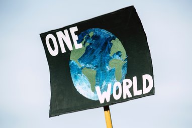 A cardboard campaign sigh that reads "One World" and an image of the Earth in the middle