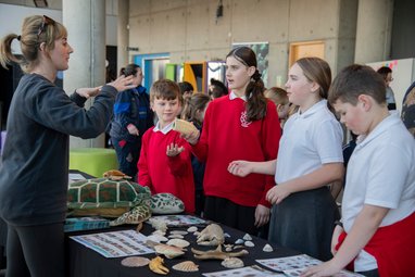 Students learning about various marine artifacts like seashells and fossils at a Marine Conservation Stall.