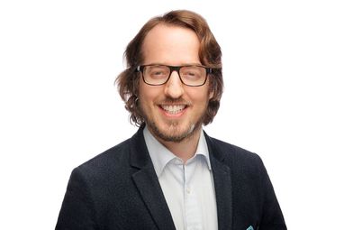 Trustee Martin Koehring smiles against a white background. He is in formal business wear - a white shirt and black suit jacket.
