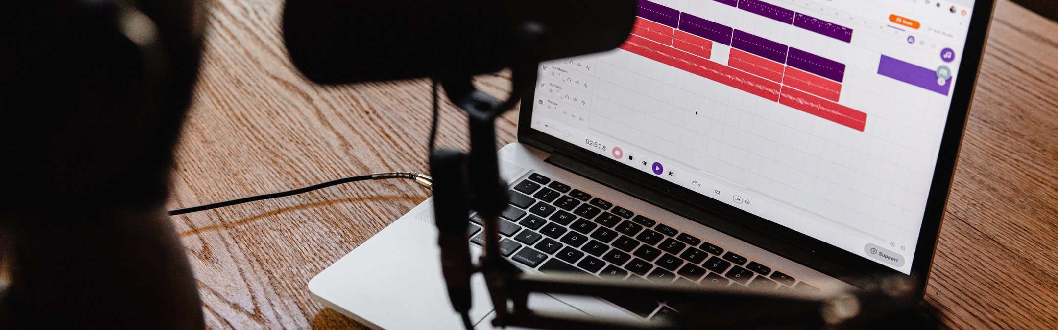 A female sits at a desk. On the desk is a laptop, and next to the laptop is a podcast microphone.