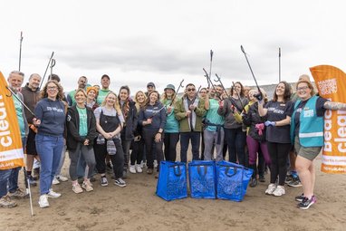 Great British Beach Clean 2025 holiday cottages group shot featuring around two dozen smiling people holding up litter grabs.