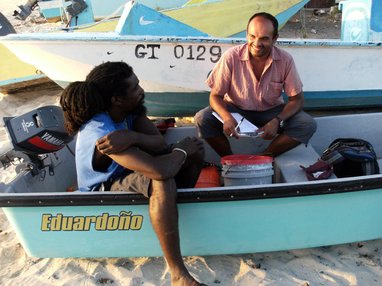 2 men talking while sitting in a boat on a beach