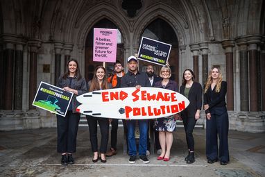 Members of the Marine Conservation Society team stand with other NGOs outside Westminster holding a surf board reading 'end sewage pollution'.