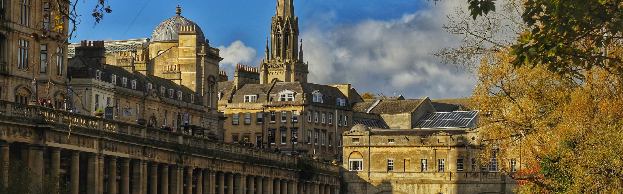 An eye-level, medium shot showing the historic Pulteney Bridge and the River Avon in Bath, England.