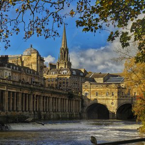 An eye-level, medium shot showing the historic Pulteney Bridge and the River Avon in Bath, England.