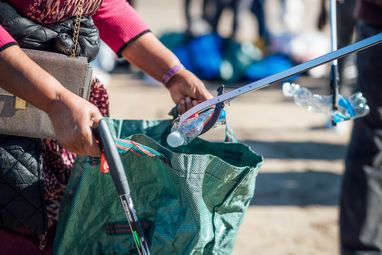 A close up of volunteers filling a bag with plastic bottles at a Scarborough beach clean.