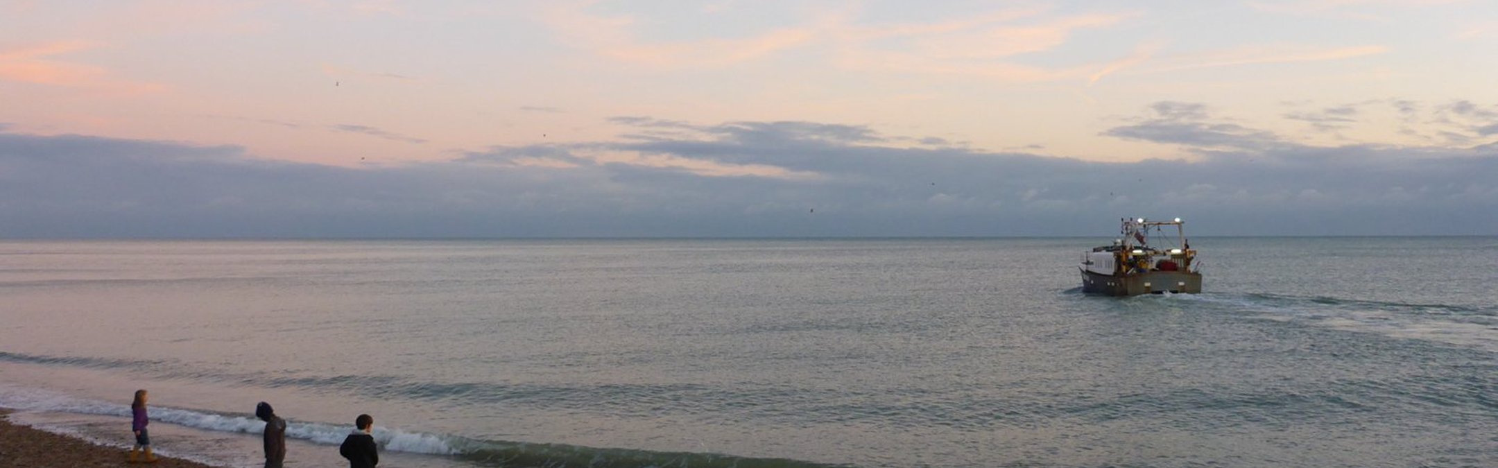 people on Hastings beach with a boat in the water