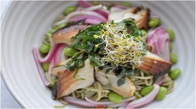 Arctic chard sits on a bed of noodles, with a salad and red onion garnish