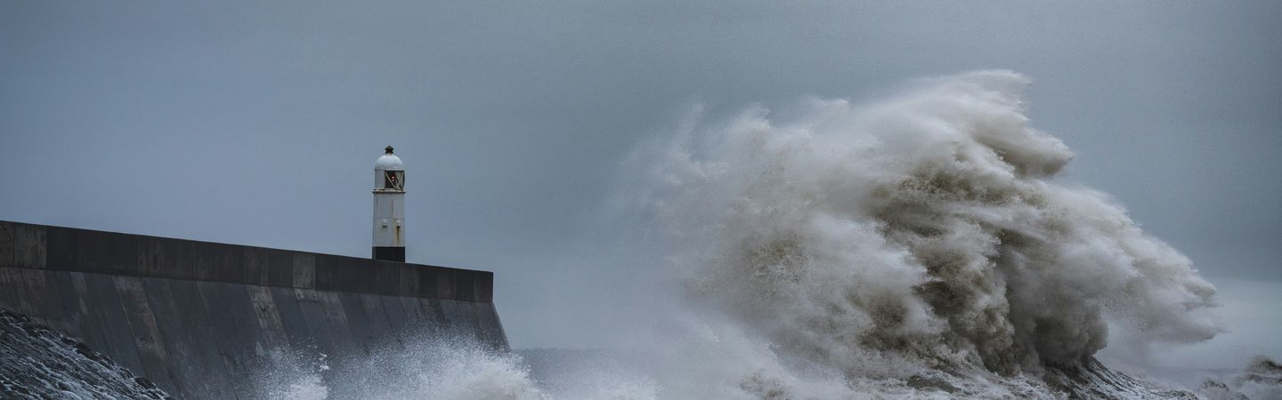 Large white waves hitting a wall at Porthcawl, Wales, with a dark grey sky above the coastline