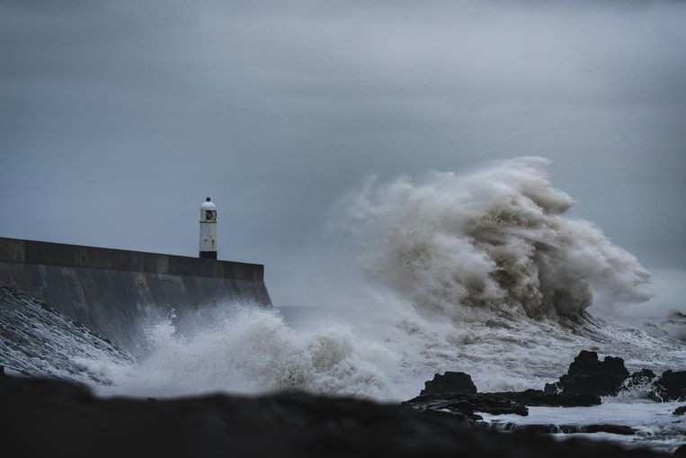 Large white waves hitting a wall at Porthcawl, Wales, with a dark grey sky above the coastline