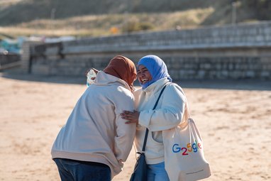 2 women laughing together on a beach.
