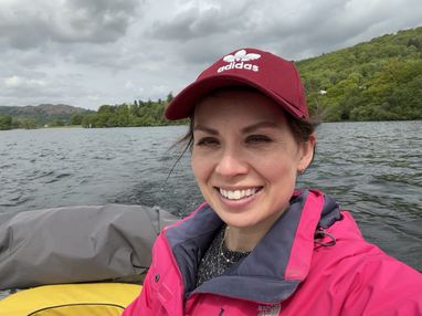 Trustee Natalie smiles from a small boat on what looks like a Loch. She is wearing a pink waterproof jacket and a burgundy cap.