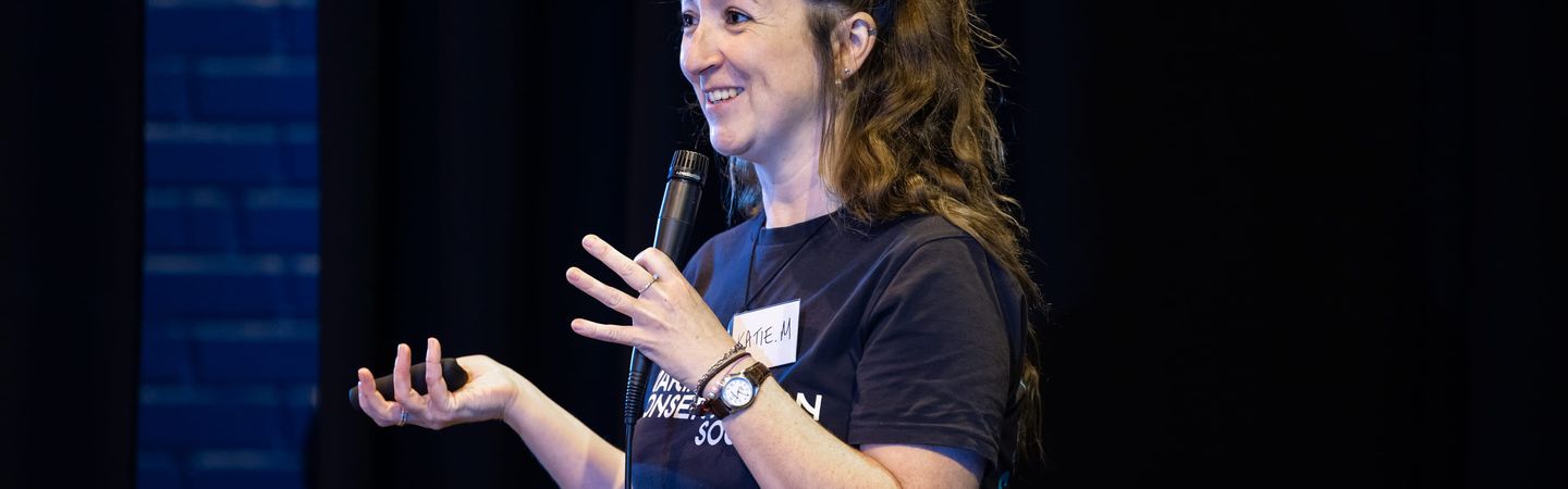 A woman holding a microphone. She is wearing a Marine Conservation Society t-shirt