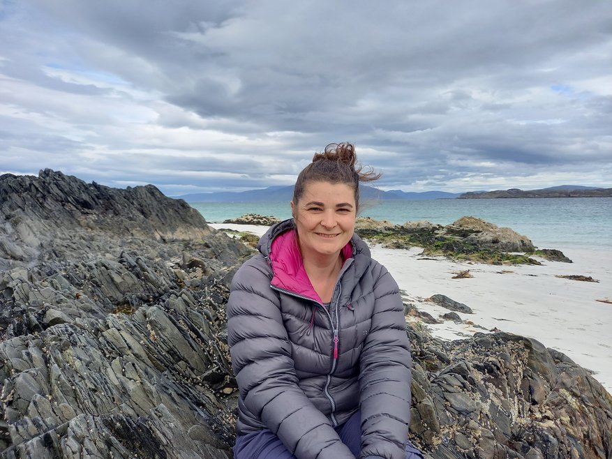 Anna Inman Restoration Forth's Shellfish Engagement Officer smiles from a beach while sat on a rock formation.