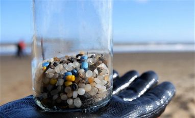 A gloved hand holds up a glass jar containing colourful plastic "nurdles", tiny pieces of plastic that were found during a beach clean