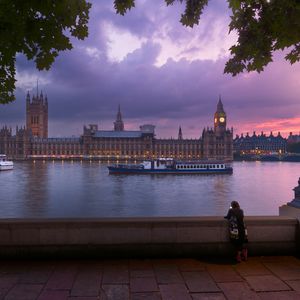 Westminster at sunset taken from the bank across the Thames. The sky is a stunning purple pink and an ornate lamp is lit in the foreground.
