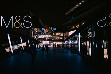 A wide-angle, night-time shot of a modern, sleek pedestrian walkway flanked by glowing storefronts.