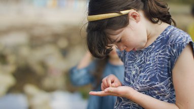A girl studying a tiny shell she has in the palm of her hand