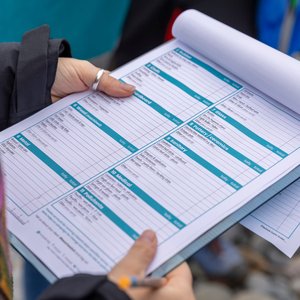 A close-up shot of a person holding a clipboard with a Marine Conservation Society beach clean survey form. The user's hands and a pen are visible as they potentially make notes on the form.