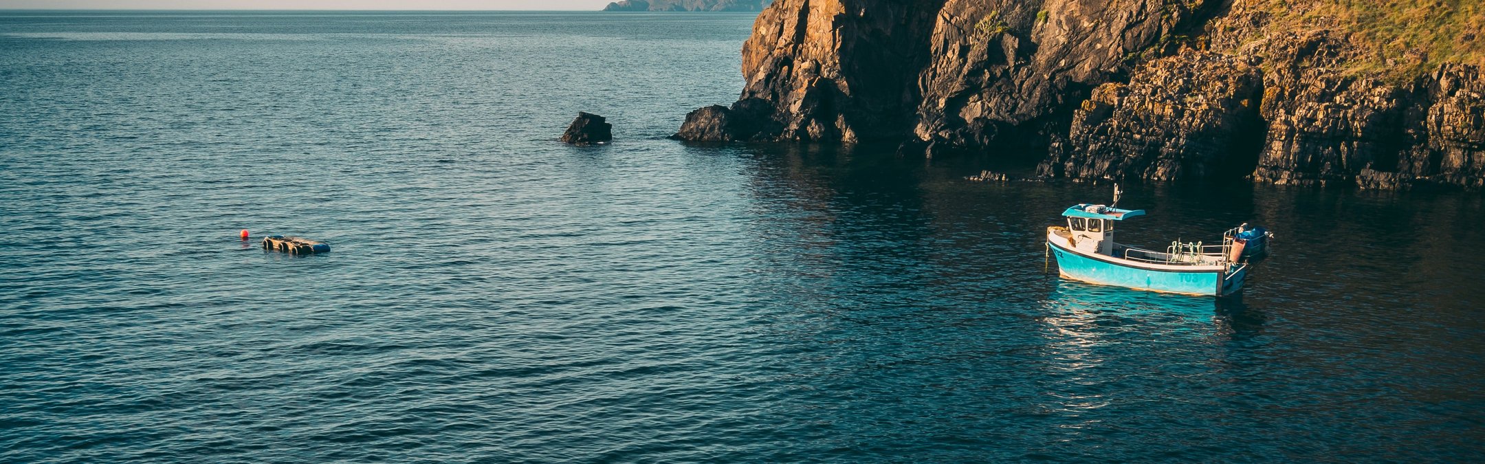 A small fishing boat is pictured leaving Abercastle Harbour. The water is a deep blue and there are craggy rocks to the right of the photo.