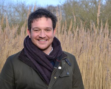 Professor Ben Garrod smiles at the camera with a reed bed backdrop.