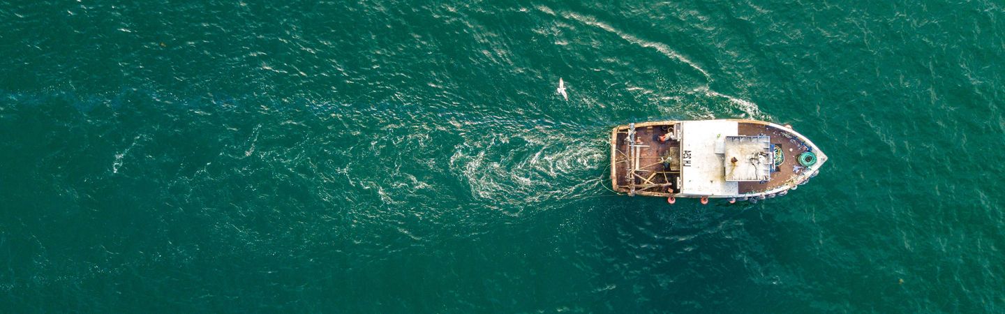 A small fishing trawler seen from a birds-eye-view over a deep blue ocean.