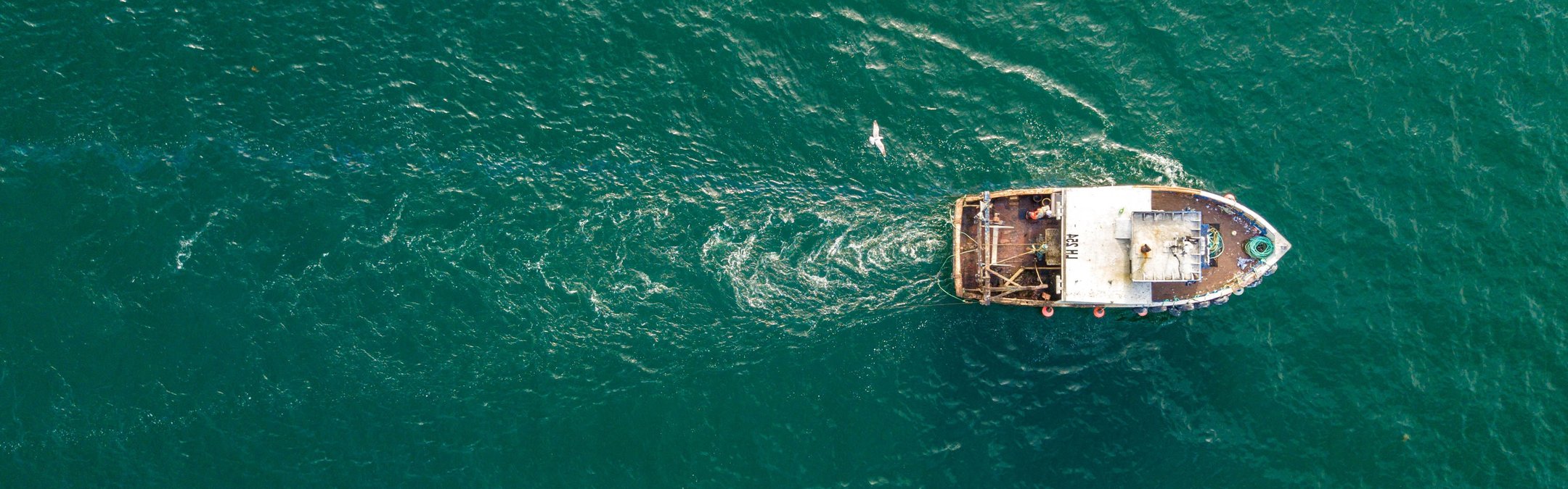A small fishing trawler seen from a birds-eye-view over a deep blue ocean.