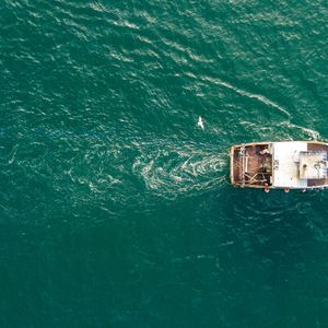 A small fishing trawler seen from a birds-eye-view over a deep blue ocean.