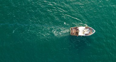 A small fishing trawler seen from a birds-eye-view over a deep blue ocean.