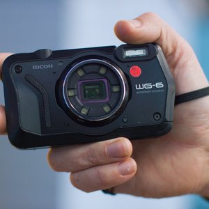 A digital camera being held up by a hand