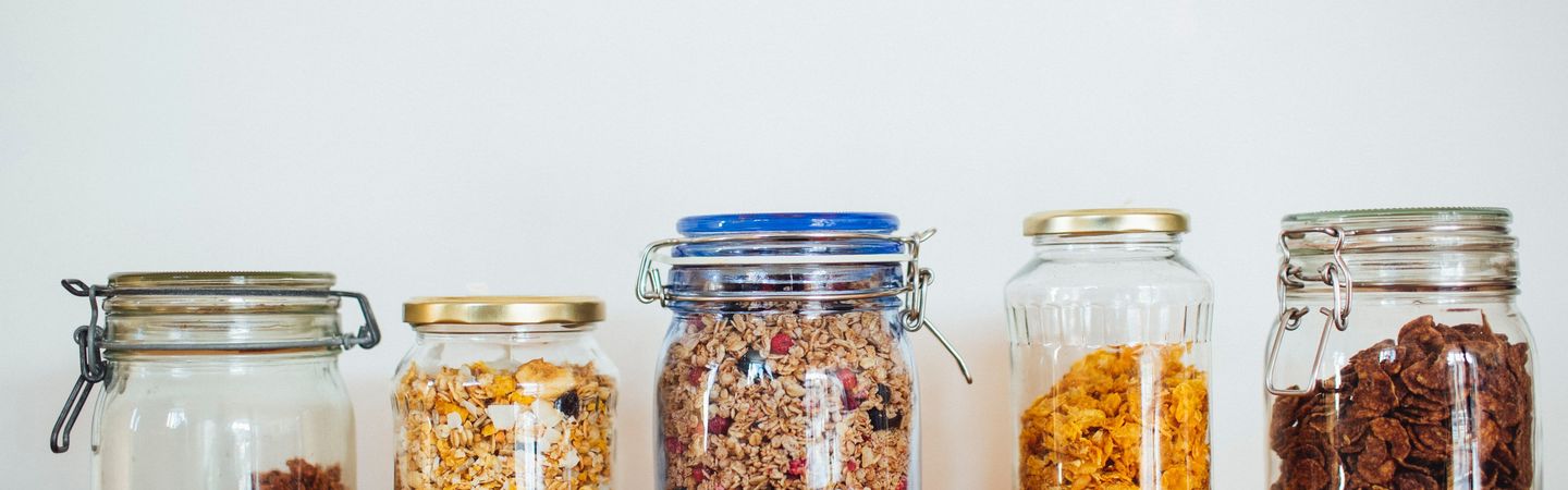 A row of glass jars on a shelf filled with different types of cereal