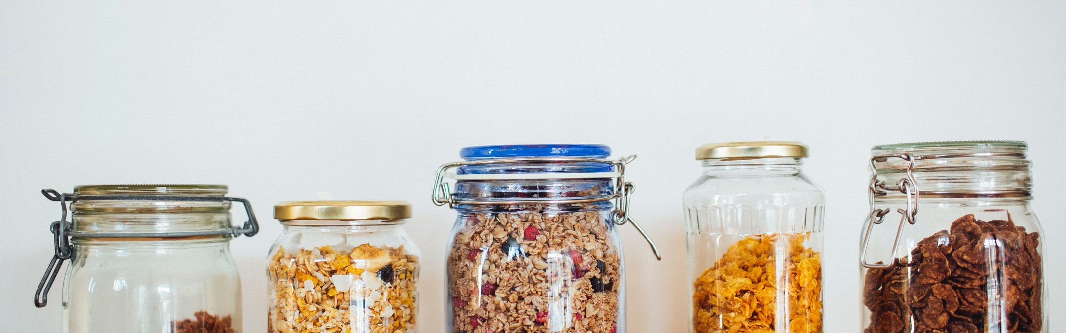 A row of glass jars on a shelf filled with different types of cereal