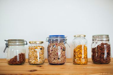 A row of glass jars on a shelf filled with different types of cereal