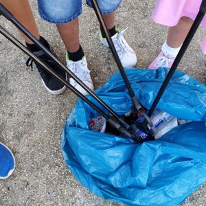 A group of children are using litterpickers to put rubbish into a blue refuse bag. Only the children's legs and feet can be seen.