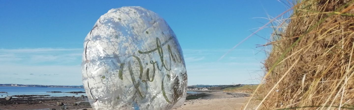 A deflated helium balloon is found on a sandy beach during a beach clean