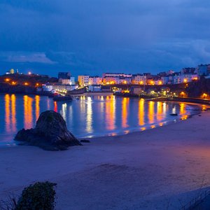 Tenby Harbour is captured at night time. The colourful lights from the buildings around the bay are reflected in the sea
