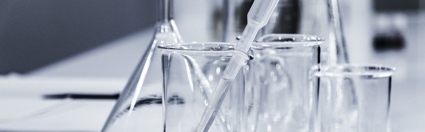 Several science beakers filled with a clear liquid and pippets, on top of a white lab table
