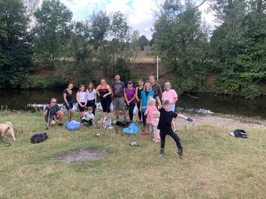A group of volunteers posing for a photo on some grass while taking part in a Source to Sea clean. A river can be seen behind them.