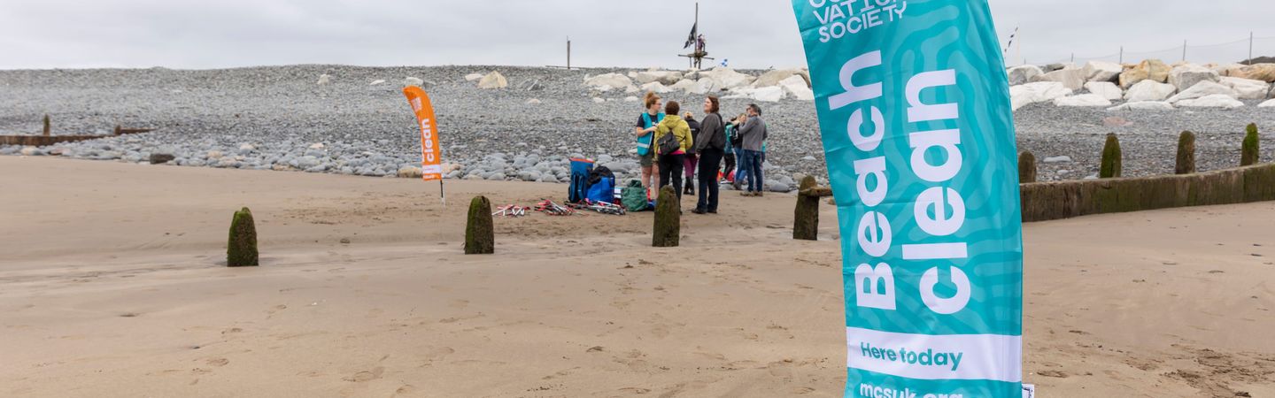 A beach with a flag in the foreground that reads "Marine Conservation Society Beach Clean"