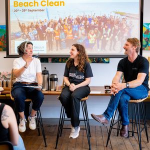 Zoe Lyons, a Marine Conservation Society staff member, and Cully from Cully and Sully, sit on stools in front of a large screen, giving a talk to an audience. All three people are smiling broadly.