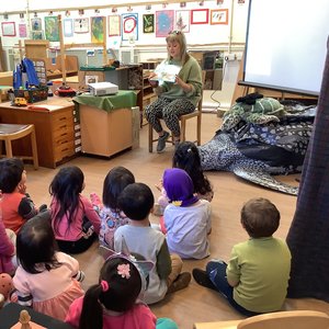 A member of Marine Conservation Society reading a book about a sea turtle to a group of young children sitting on the floor in a classroom.