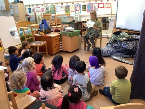 A member of Marine Conservation Society reading a book about a sea turtle to a group of young children sitting on the floor in a classroom.