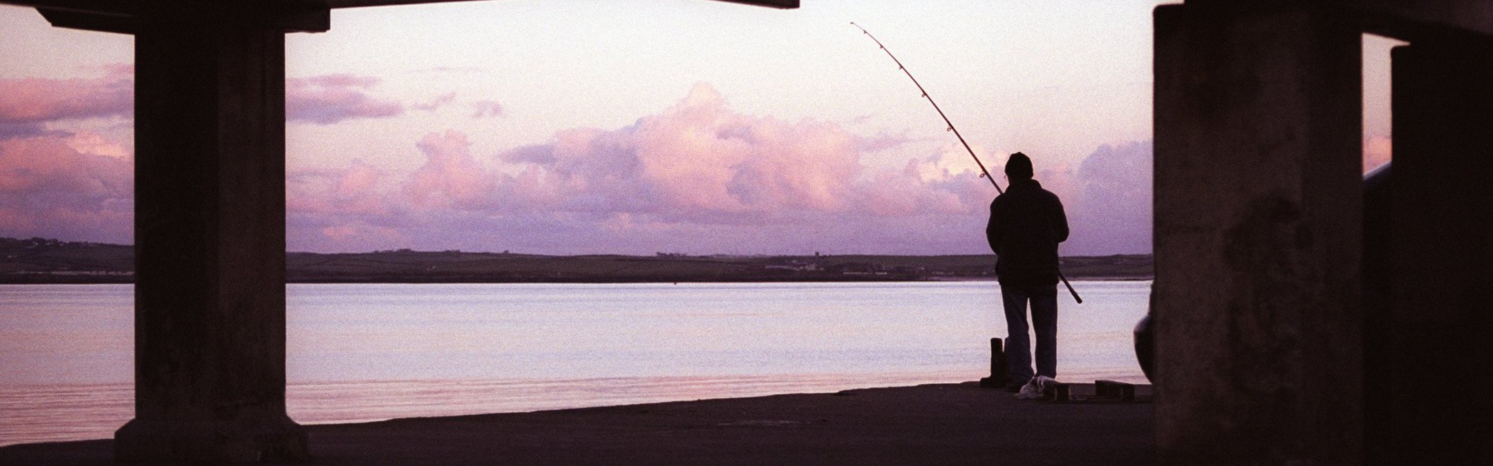 A silhouette of a lone fisherman under a pier.