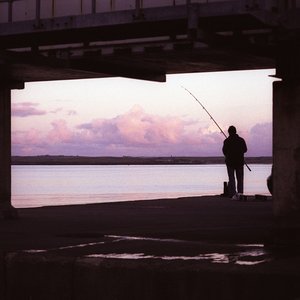 A silhouette of a lone fisherman under a pier.