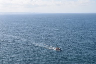 An aerial shot of the ocean, with a small fishing boat to the right of the photograph.
