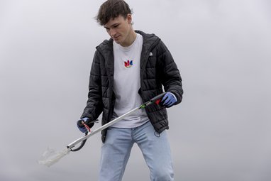 A teenage boy picking up marine litter with a litter picker. He is wearing a black coat and white t-shirt