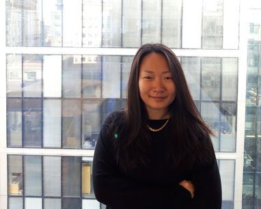 Trustee Helena Thermstrom smiles against a glass window with a city glass office block behind her. She is wearing a black jumper.