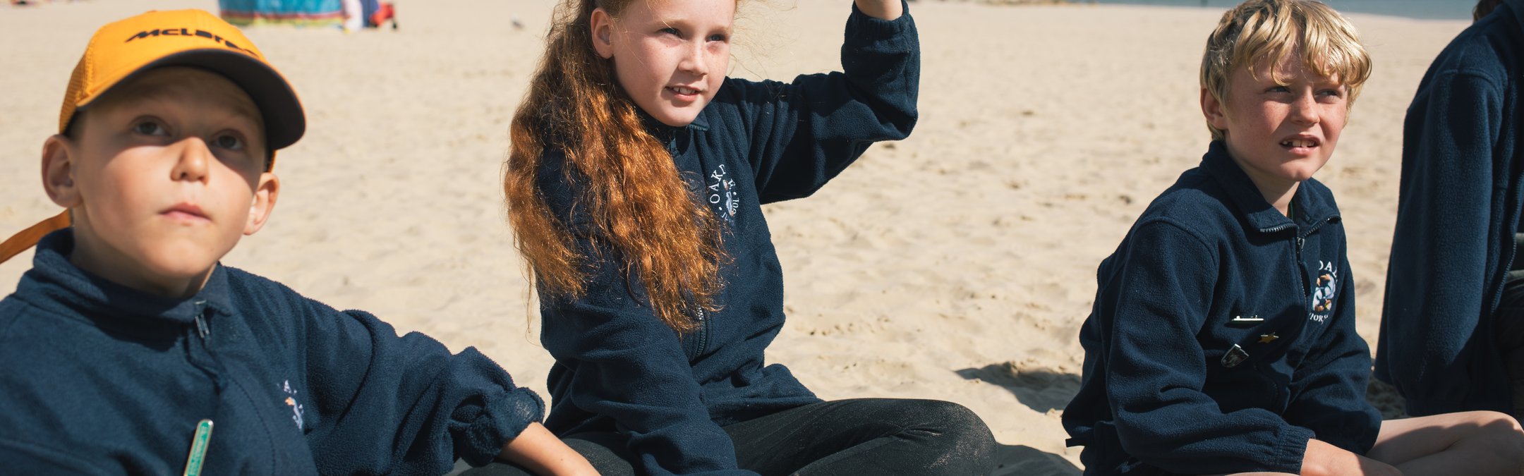 A young girl sitting on a beach with her hand up
