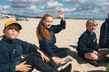A young girl sitting on a beach with her hand up
